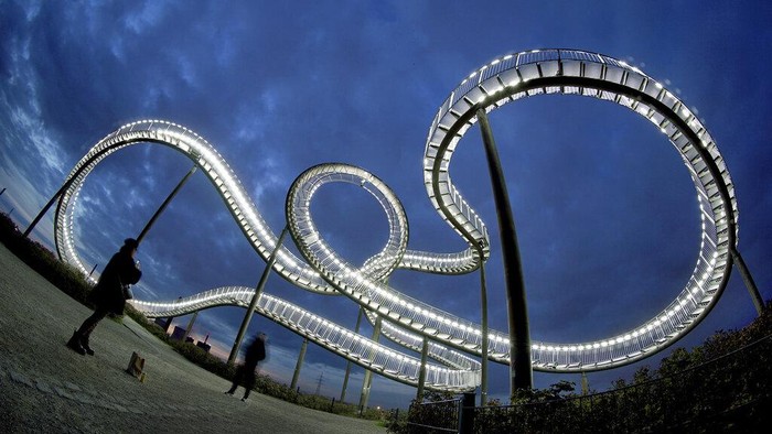 People visit the Tiger and Turtle - Magic Mountain walkable roller coaster sculpture in Duisburg, Germany, Thursday, April 4, 2024. The widely visible landmark Tiger And Turtle - Magic Mountain was built on a former dump close to the Krupp Mannesman metallurgical plant in Duisburg, one of Europes biggest locations of the steel industry. (AP Photo/Michael Sohn)