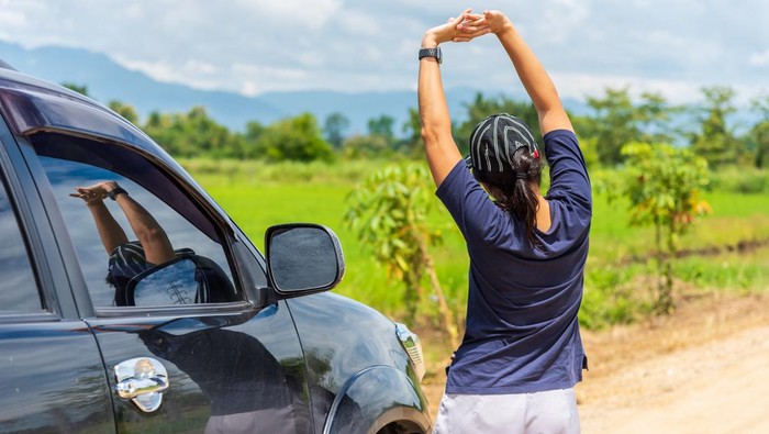 Woman driver is stretching after a long road trip drive to relieve her back pain.