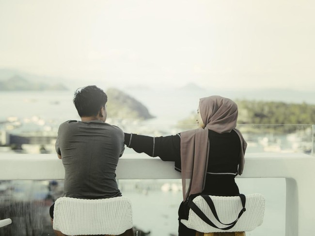 two young asian muslim couple sitting on the cafe  and looking the labuan bajo islands view on summer day