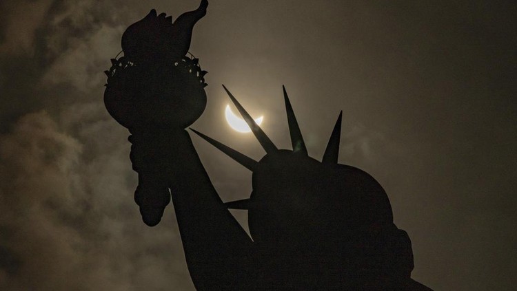 Potret Memukau Gerhana Matahari di AS dan Meksiko The moon partially covers the sun behind the Statue of Liberty during the a solar eclipse on the Liberty Island, Monday, April 8, 2024, in New York. (AP Photo/Yuki Iwamura)