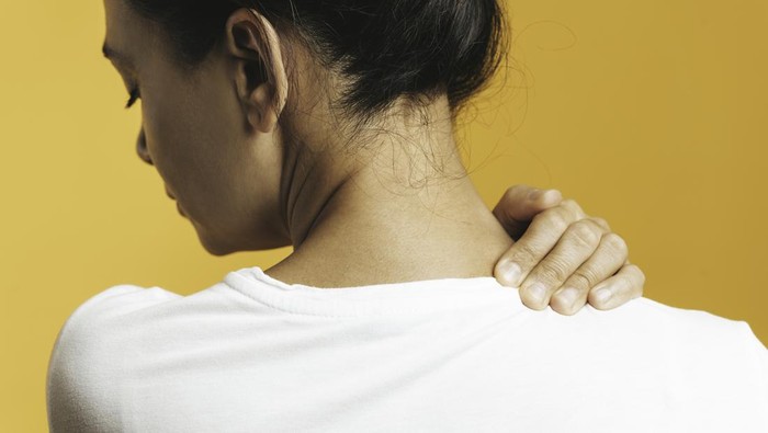 Back view of unrecognizable woman with neck pain in front of yellow background.