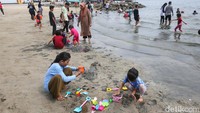 Anak-anak bermain pasir di pinggir pantai.
