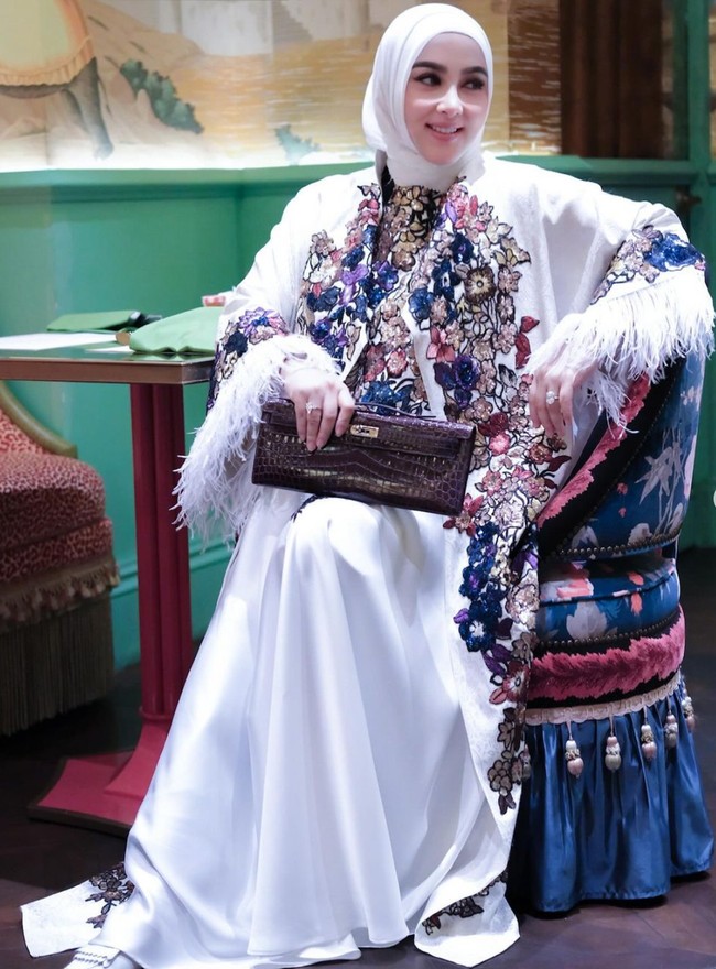 Melengkapi penampilannya, Syahrini mengenakan hijab senada dan membawa clutch berwarna coklat tua. Sambil duduk, ia tersenyum dengan mata tak menatap ke arah kamera. Foto: Instagram/@princessyahrini