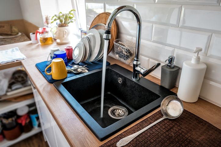 Water flowing out of a kitchen stainless steel tap into the sink. Wasting water by leaving a chrome faucet tap running