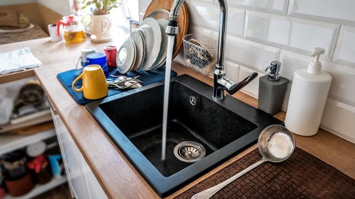 Water flowing out of a kitchen stainless steel tap into the sink. Wasting water by leaving a chrome faucet tap running