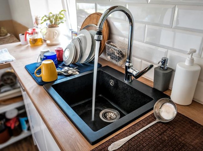 Water flowing out of a kitchen stainless steel tap into the sink. Wasting water by leaving a chrome faucet tap running