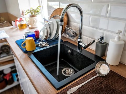 Water flowing out of a kitchen stainless steel tap into the sink. Wasting water by leaving a chrome faucet tap running