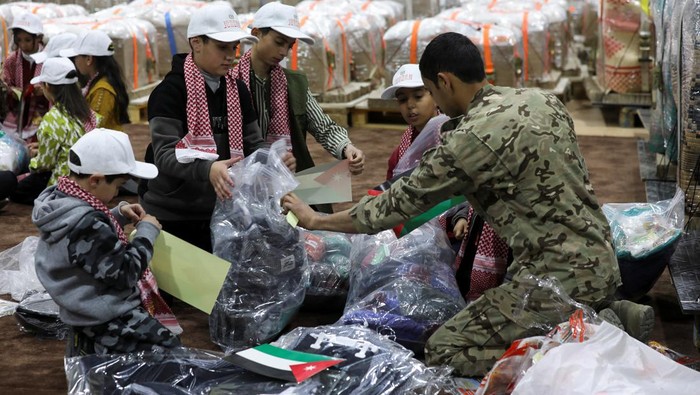 Militer Yordania Terjunkan Paket Lebaran ke Gaza Children help a military personnel packing clothes aid that is scheduled to be airdropped over Gaza, ahead of the Muslim celebration of Eid al-Fitr, in Zarqa , Jordan April 7, 2024. REUTERS/Alaa Al Sukhni