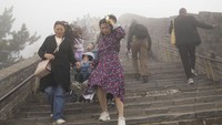 Pengunjung menggendong seorang anak di kereta dorong menuruni tangga di hamparan Tembok Besar Tiongkok Badaling di pinggiran kota Beijing, Sabtu (13/4/2024).