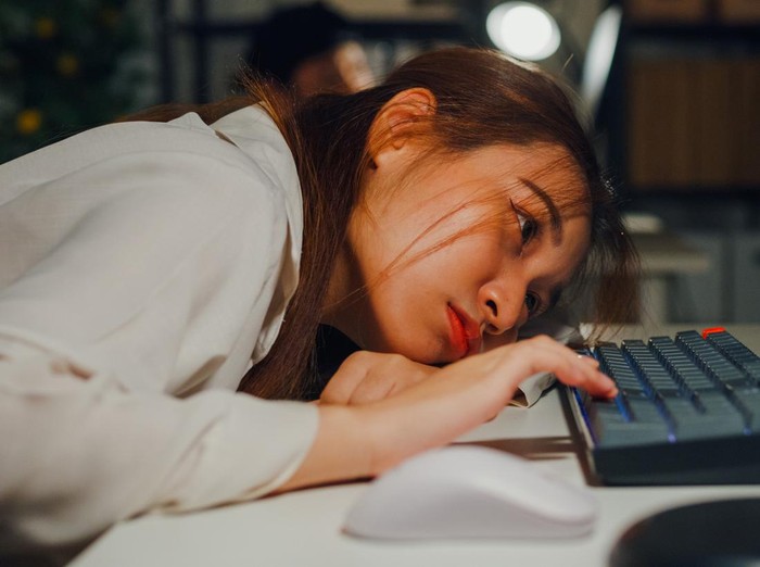 2119959290 Closeup of Asian woman appears deeply fatigued and stressed while working on laptop in office night, highlighting issues of overwork and employee burnout. ESG sustainable business office concept.