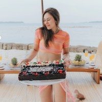 Berpose bersama kue ulang tahunnya, Wulan tampil dengan setelan berwarna oranye. setelan berupa crop top dan rok berbelahan tinggi itu tampak memperlihatkan perut ratanya dengan jelas. Foto: Instagram/@wulanguritno
