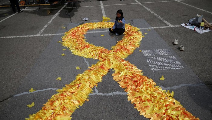 People pay their silent tributes behind a large yellow colored ribbon dedicated to victims of the sunken Sewol ferry disaster that killed 304 people, mostly school students, during a ceremony to commemorate its tenth anniversary in Ansan, South Korea, April 16, 2024.     REUTERS/Kim Hong-Ji