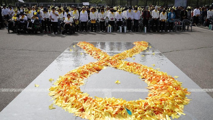 People pay their silent tributes behind a large yellow colored ribbon dedicated to victims of the sunken Sewol ferry disaster that killed 304 people, mostly school students, during a ceremony to commemorate its tenth anniversary in Ansan, South Korea, April 16, 2024.     REUTERS/Kim Hong-Ji