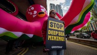 Massa menunjukkan poster yang tertuliskan Stop Deep Sea Mining di sebelah gurita raksasa.  