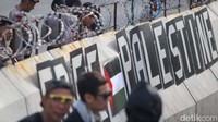Tulisan FREE PALESTINE juga terlihat telah dipasang di pembatas beton yang ada di lokasi. Beberapa peserta aksi tampak mengibarkan bendera Palestina.