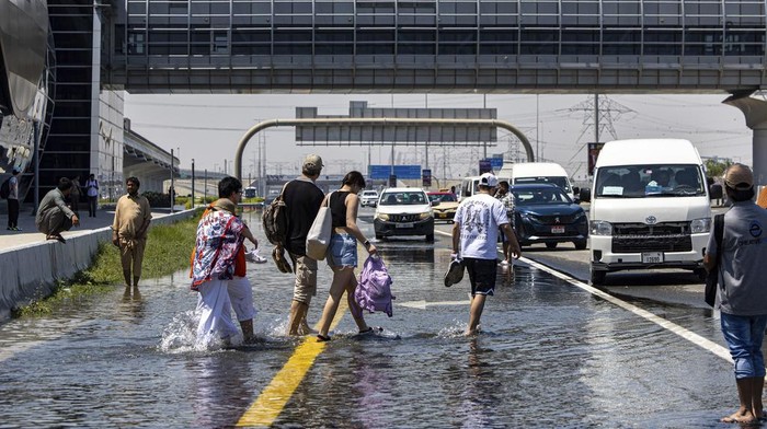Mobil Terjebak Banjir di Dubai, Penumpang Keluar dan Jalan Kaki People walk through floodwater caused by heavy rain while waiting for transportation on Sheikh Zayed Road highway in Dubai, United Arab Emirates, Thursday, April 18, 2024. The United Arab Emirates attempted to dry out Thursday from the heaviest rain the desert nation has ever recorded, a deluge that flooded out Dubai International Airport and disrupted flights through the world's busiest airfield for international travel. (AP Photo/Christopher Pike)