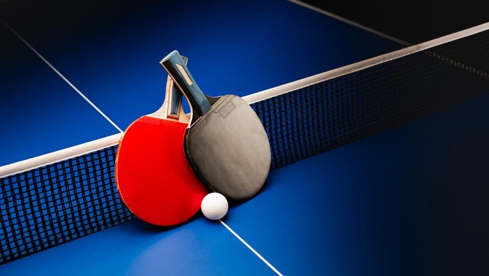 Two table tennis rackets and balls on a blue table with net.