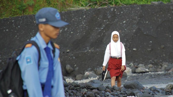 Seorang warga menggendong siswa sekolah dasar (SD) untuk berangkat sekolah melintasi daerah aliran sungai (DAS) Kali Regoyo di Desa Jugosari, Kecamatan Candipuro, Lumajang, Jawa Timur, Senin (22/4/2024). Sebanyak 40 siswa SDN Jugosari 3 terpaksa menyeberangi sungai disebabkan jembatan limpas sebagai akses utama menuju sekolah terdampak banjir lahar hujan Semeru. ANTARA FOTO/Irfan Sumanjaya/rwa.