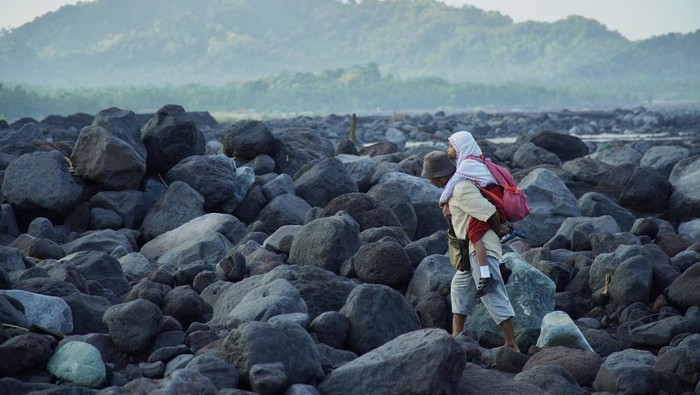 Seorang warga menggendong siswa sekolah dasar (SD) untuk berangkat sekolah melintasi daerah aliran sungai (DAS) Kali Regoyo di Desa Jugosari, Kecamatan Candipuro, Lumajang, Jawa Timur, Senin (22/4/2024).  Sebanyak 40 siswa SDN Jugosari 3 terpaksa menyeberangi sungai disebabkan jembatan limpas sebagai akses utama menuju sekolah terdampak banjir lahar hujan Semeru. ANTARA FOTO/Irfan Sumanjaya/rwa.