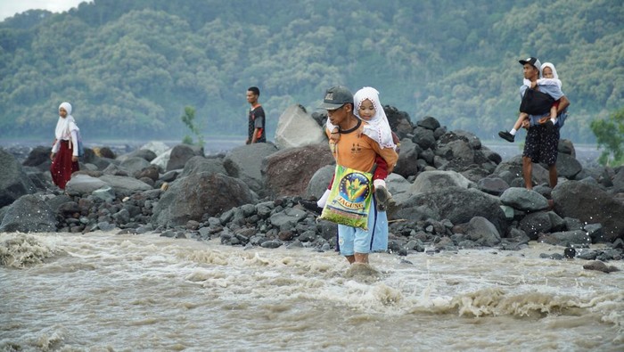 Seorang warga menggendong siswa sekolah dasar (SD) untuk berangkat sekolah melintasi daerah aliran sungai (DAS) Kali Regoyo di Desa Jugosari, Kecamatan Candipuro, Lumajang, Jawa Timur, Senin (22/4/2024).  Sebanyak 40 siswa SDN Jugosari 3 terpaksa menyeberangi sungai disebabkan jembatan limpas sebagai akses utama menuju sekolah terdampak banjir lahar hujan Semeru. ANTARA FOTO/Irfan Sumanjaya/rwa.