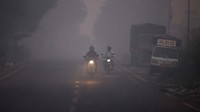Para pengendara melintas di jalan yang tertutup asap kebakaran sampah. 