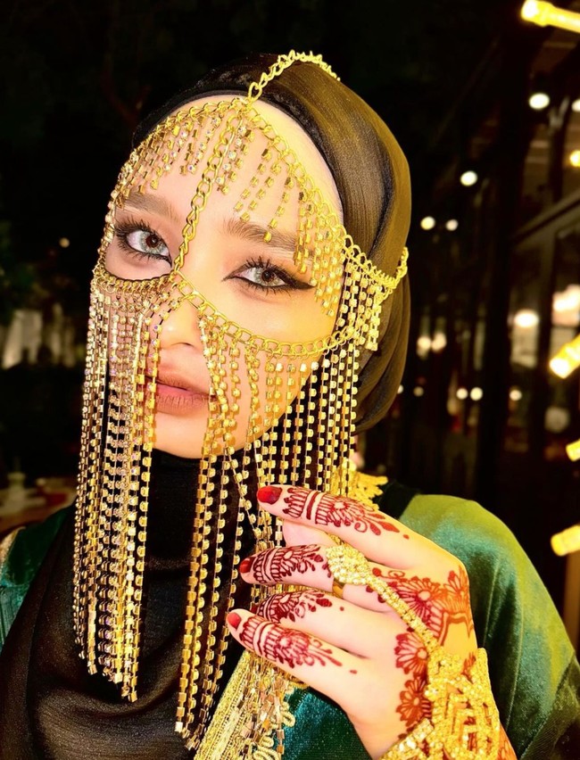 Totalitas menjelma menjadi wanita Arab, Inara tampak mengenakan cadar rantai berwarna gold dan Henna di tangannya. Riasan wajahnya, terutama bagian matanya dibuat dramatis menggunakan eyeliner pada bagian atas dan bawah matanya. Foto: Instagram/@mommy_starla