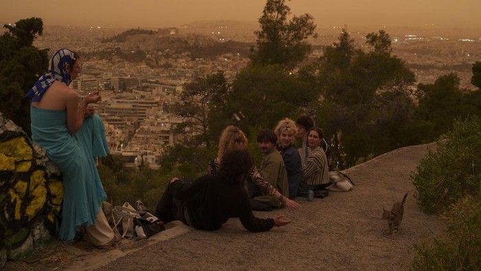 Potret Langit Yunani Berubah Oranye Gegara Debu Gurun Sahara Tourists walk at the Lycabettus hill as the city of Athens with the ancient Acropolis hill is seen at the background, on Tuesday, April 23, 2024. The Acropolis and other Athens landmarks took on Martian hues Tuesday as stifling dust clouds blown across the Mediterranean Sea from North Africa engulfed the Greek capital. (AP Photo/Petros Giannakouris)