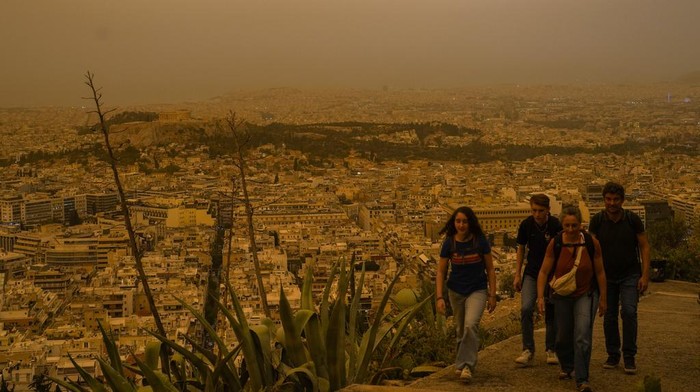 Tourists walk at the Lycabettus hill as the city of Athens with the ancient Acropolis hill is seen at the background, on Tuesday, April 23, 2024. The Acropolis and other Athens landmarks took on Martian hues Tuesday as stifling dust clouds blown across the Mediterranean Sea from North Africa engulfed the Greek capital. (AP Photo/Petros Giannakouris)