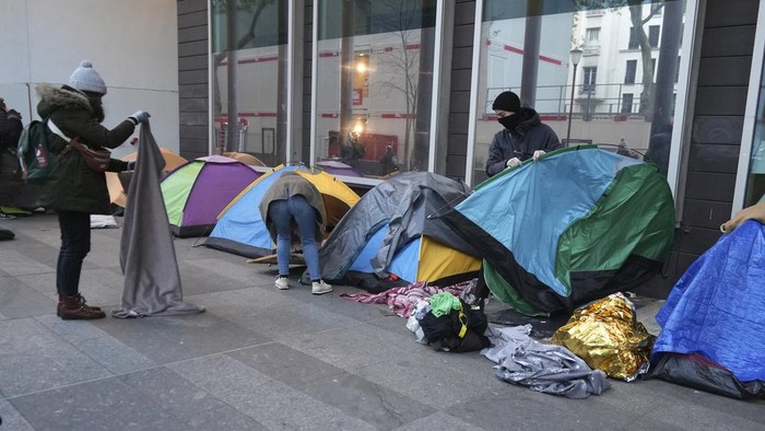 A police officers checks a migrants tent in a makeshift camp, early Tuesday, April 23, 2024 in Paris. French police officers have evicted migrants from a makeshift camp in Paris a few steps away from the Seine River, as similar operations have been carried out by authorities ahead of the Olympics. (AP Photo/Nicolas Garriga)