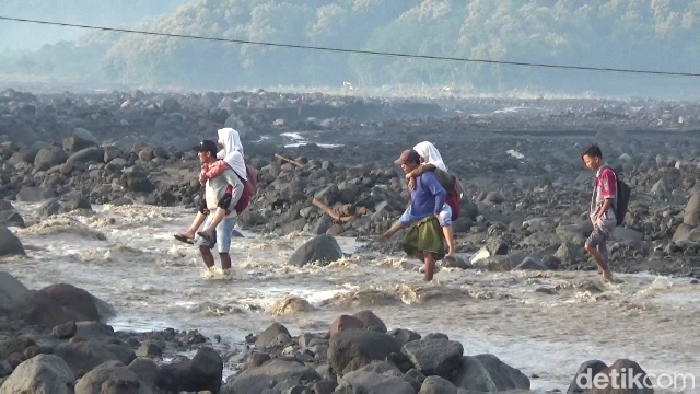 Ayah gendong anaknya menyeberangi aliran lahar Semeru demi ke sekolah.