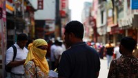 Seorang wanita memakai penutup wajah untuk menghindari sengatan panas matahari langsung.  