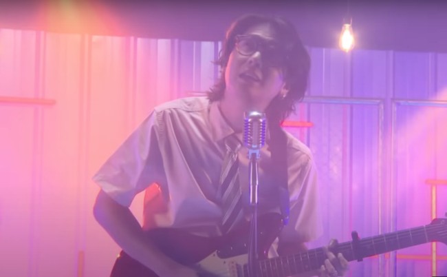 Iqbaal tampil rapih mengenakan kemeja putih dan celana panjang. Ia juga melengkapi penampilannya dengan kaca mata dan dasi bermotif. Foto: YouTube/Iqbaal Ramadhan