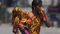 Seorang wanita India yang menggendong seorang anak menggunakan sebagian sarinya untuk melindungi anaknya dari sinar matahari di Hyderabad, India, Rabu (1/5/2024). (AP Photo/Mahesh Kumar A.)  