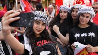 Di Beirut, demonstran pro-Palestina bercampur dengan pekerja menuntut diakhirinya kesengsaraan ekonomi. Wanita muda pendukung partai Komunis Lebanon berfoto selfie dan menunjukkan tanda kemenangan. AP/Hussein Malla