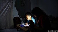 Seorang ibu menemani buah hatinya yang sedang mengikuti pembelajaran jarak jauh. Dia menemani sambil menyalakan senter handphone untuk menerangi anaknya yang sedang belajar.  