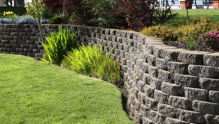 Well landscaped wall of cement cobblestone bricks with grass and ornamental plants