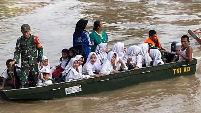 Anggota Babinsa Koramil 406-03/ Rupit Kodim 0406/Lubuk Linggau membantu anak sekolah menyeberangi Sungai Rupit.
