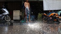 Warga menyemprotkan air di depan kiosnya untuk mengusir hawa panas.