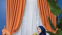 Tampil cantik dan keren, Irish Bella berpose dengan secangkir teh di depan gorden berwarna cerah yang disukainya. Foto: Instagram @_irishbella_