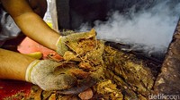 Perajin memasukkan batok kelapa kedalam tungku pemanggang ikan.