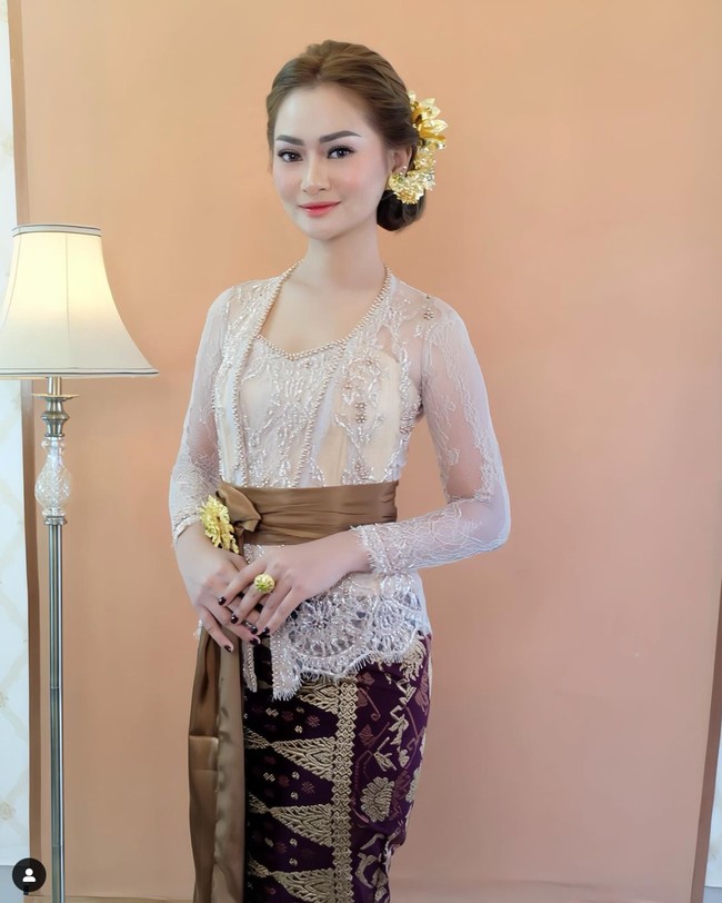 Nindy tampil anggun dalam balutan kebaya Bali berwarna krem dan kain songket berwarna ungu gelap dan coklat muda. Penampilannya itu kemudiann dilengkapi dengan ikat pinggang berwarna coklat. Dengan rambut tersanggul dan pulasan makeup natural glow, penampilan Nindy semakin terlihat ayu. Foto: Instagram/@nindypricilia