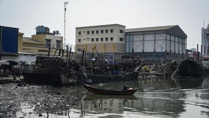 Pekerja menggunakan sampan melintas di depan bangkai kapal yang hangus terbakar di Pelabuhan Muara Baru, Jakarta, Senin (6/5/2024). Setelah dinyatakan padam oleh Suku Dinas Penanggulangan Kebakaran dan Penyelamatan (Gulkarmat) Jakarta Utara pada, Minggu (5/5) malam, satu dari tiga bangkai kapal kembali terbakar pada, Senin (6/6) pagi akibat hembusan angin dan sebagian besar kapal itu berbahan fiber yang mudah terbakar. ANTARA FOTO/Erlangga Bregas Prakoso/YU