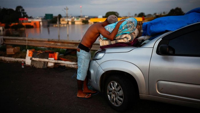 Men fold a blanket as they camp on the road near a flooded street in Eldorado do Sul, in Rio Grande do Sul, Brazil, May 6, 2024. REUTERS/Amanda Perobelli