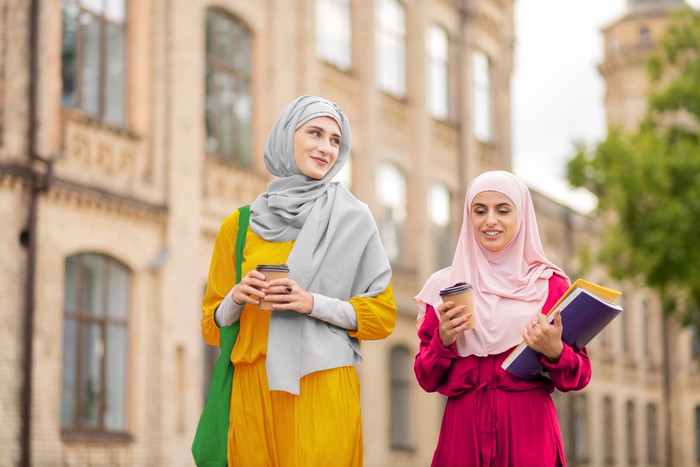 Drinking and walking. Muslim students wearing bright hijabs drinking coffee and walking to university