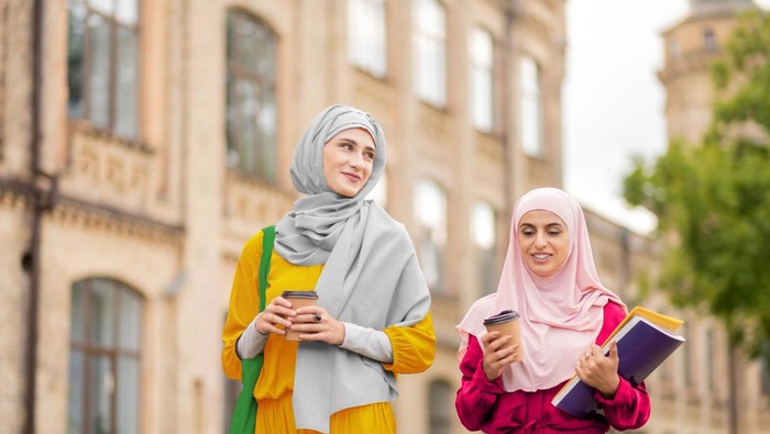 Drinking and walking. Muslim students wearing bright hijabs drinking coffee and walking to university