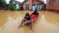 Dua orang anak melintasi banjir menggunakan perahu.