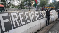 Tulisan FREE PALESTINE juga terlihat telah dipasang di pembatas beton yang ada di lokasi. Beberapa peserta aksi tampak mengibarkan bendera Palestina.