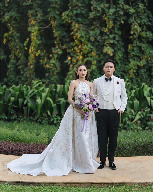 Mempelai pria, Rizky Febian, tampil elegan dalam balutan tailcoat tuxedo putih yang dipadankan celana hitam, dari koleksi Henri Winata. Foto: Instagram/@axioo @thebridestory @hiantjen @dhirmanputra