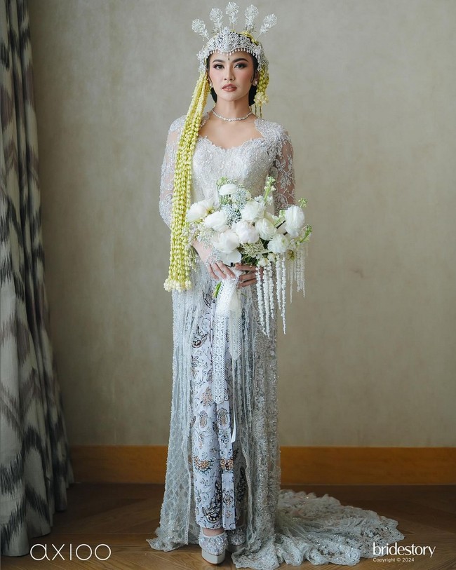 Untuk akad nikah, penyanyi 24 tahun ini kembali mempercayakan Asky Febrianti untuk membuatkan busana. Kebaya putih Mahalini tampak mewah dengan perpaduan berbagai ornamen seperti sequin, payet, kristal dan bordiran. Kebaya modern dengan garis leher heart-shaped itu dipadukan dengan kain Batik bernuansa hitam-putih. Foto: Instagram/@axioo @thebridestory @hiantjen