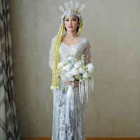 Untuk akad nikah, penyanyi 24 tahun ini kembali mempercayakan Asky Febrianti untuk membuatkan busana. Kebaya putih Mahalini tampak mewah dengan perpaduan berbagai ornamen seperti sequin, payet, kristal dan bordiran. Kebaya modern dengan garis leher heart-shaped itu dipadukan dengan kain Batik bernuansa hitam-putih. Foto: Instagram/@axioo @thebridestory @hiantjen